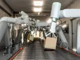 Wiele ramion robotów współpracujących chwyta kartony na linii produkcyjnej.
