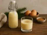 Szklanka i butelka z kremowym ajerkoniakiem, obok miseczka z cynamonem i jajka. Idealny na zimowe wieczory.