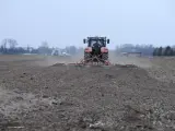 Czerwony traktor z agregatem uprawowym przygotowuje pole pod zasiew. Dzierżawa ziemi w pełni.