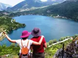 Coppia ammira un lago a forma di cuore, circondato da montagne verdi e alberi.