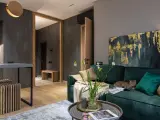 Nowoczesny salon z butelkową zielenią farby do ścian. Kot odpoczywa na kanapie, obok wazon z kwiatami.