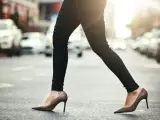 Kobieta w wąskich czarnych spodniach i brązowych szpilkach przechodzi przez ulicę. Idealne buty do wąskich spodni damskich.