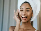 Une jeune femme avec une serviette sur la tête, appliquant un soin sur son visage. Elle semble heureuse, peut-être grâce aux bienfaits du collagène ou de l'acide hyaluronique.