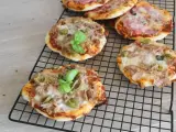 Kilka pysznych pizzett z tuńczykiem, oliwkami i bazylią na czarnej kratce.