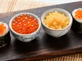 Dwa sushi rolki z pomarańczowym ikrą masago i miseczki z ikrą.