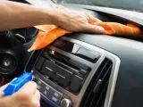En hand sprayar och torkar av bilens instrumentbräda med en orange trasa. Det ser ut som en magisk rengöring för att få bilen skinande ren.