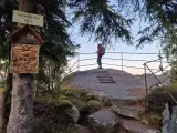 Widok na szczyt Kamienna Góra (704 m). Turystka podziwia panoramę, a obok drzewa ozdobiona kapliczka.