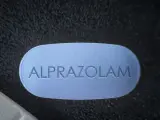 Niebieska tabletka z napisem "ALPRAZOLAM" leży obok białej. Uważaj na niebezpieczne skutki połączenia xanax i alkohol.