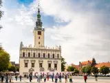 Rynek w Chełmnie z ratuszem i tablicą z napisem "Chełmno". Ludzie spacerują, podziwiając atrakcje miasta.