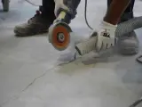 Trabajador usa una amoladora para hacer una solera de hormigón sobre tierra, aspirando el polvo.