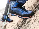 Close-up of a blue and black hiking boot with orange accents, gripping a rocky surface.