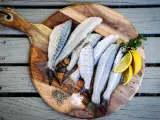 Plusieurs poissons frais sur une planche à découper en bois avec du sel, du poivre et des quartiers de citron.