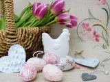 Wielkanocne dekoracje: koszyk z tulipanami, ceramiczna kurka, ozdobne jajka i serca.