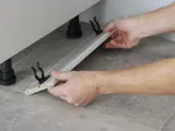 Mani che assemblano uno zoccolo cucina in alluminio, mostrando come tagliare e fissare i supporti.