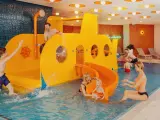 Rodzina bawi się w hotelu z aquaparkiem dla dzieci w górach. Żółta łódź podwodna ze zjeżdżalnią to centrum wodnych atrakcji.