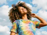 Une femme souriante aux cheveux bouclés, sous un ciel bleu nuageux. Elle porte un t-shirt tie-dye coloré. Une belle image pour apprendre comment rendre une photo flou.