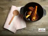 Souris d'agneau à la cocotte en fonte, tendres et savoureuses, prêtes à être dégustées. Une cuillère en bois et une serviette rose complètent la scène.