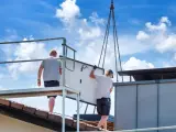 Dwaj pracownicy montują panel fotowoltaiczny na dachu. Ciężka praca i ryzyko wypadku to negatywne skutki fotowoltaiki, które często się pomija.