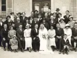Un groupe pose pour une photo de mariage, peut-être pour un registre mariage. La mariée porte une robe blanche et un voile.