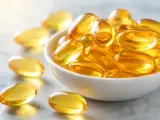 Capsule dorate piene di olio, che ricordano le proprietà omega 3, in una ciotola bianca e sparse sul piano.