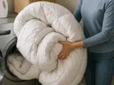 Persona mete un edredón blanco en la lavadora. Aprende como lavar un plumas a mano para mantenerlo esponjoso.
