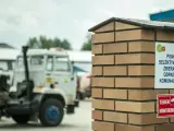 Tablica informuje, co to jest pszok – punkt selektywnego zbierania odpadów komunalnych. W tle widać ciężarówki.