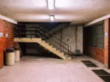 Betonowa suterena z ceglanymi ścianami, schodami i dwoma koszami na śmieci.