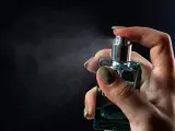 Dłoń trzymająca buteleczkę perfum i rozpylająca mgiełkę.