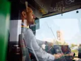 Skupiony kierowca autobusu prowadzi pojazd, trzymając kierownicę. Widać jego profil i fragment deski rozdzielczej.