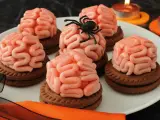 Gruselige Halloween-Nachspeise: Kekse mit Gehirn-förmiger rosa Glasur, dekoriert mit einer Spinne. Kerzen leuchten im Hintergrund.