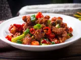 Chrupiący kurczak po kantonsku z papryczkami chili i zieloną cebulką na białym talerzu.