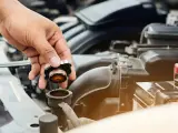 Hand removing radiator cap. This image might be relevant when researching radiator hose replacement cost.