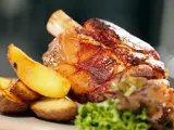Codillo de cerdo asado, crujiente y jugoso, acompañado de patatas gajo doradas y una guarnición verde.