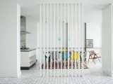 Elegante solución para dividir salón en dos ambientes. Cocina moderna y comedor con sillas de colores, separados por una celosía blanca.