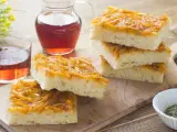 Focaccia con cipolle dorate e soffice, servita su un tagliere di legno con un bicchiere di vino rosato.
