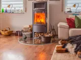 Un poêle bouilleur mixte crépite, réchauffant le salon où un chien dort paisiblement sur un tapis. Bois et paniers complètent ce tableau cosy.