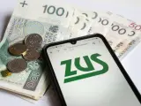 Złotówki i monety obok telefonu z logo ZUS. Może to być związane z wnioskiem o zasiłek opiekuńczy.