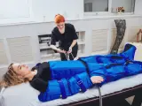Kobieta w salonie piękności przechodzi zabieg drenażu limfatycznego. Terapeuta przygotowuje urządzenie do masażu uciskowego.