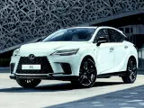 Biały Lexus RX500h z czarnymi felgami stoi przed nowoczesnym budynkiem o geometrycznej fasadzie.