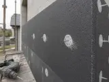 Na budowie trwa kołkowanie styropianu. Widać szarą płytę izolacyjną przymocowaną do ściany białymi kołkami. Obok leży wiertarko-wkrętarka.