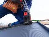Pracownik montuje blachodachówkę, narzędzia i pasy robocizny dachu za m2.