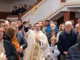 Kapłan błogosławi wiernych podczas liturgii Wielkiej Soboty, unosząc kropidło. W tłumie widać ludzi z zapalonymi świecami.