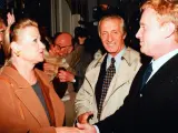 Monika Dzienisiewicz-Olbrychska w brązowym płaszczu wita się z mężczyznami. W tle widać kamery i innych ludzi.