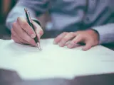 Mano firmando un contrato de reserva de vivienda. El documento se extiende sobre una mesa, con un bolígrafo en acción.