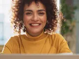 Lächelnde Frau mit Locken am Laptop, bereit für ihre Bewerbung als studentische Hilfskraft.