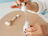 Dłoń z ciemnym lakierem do paznokci aplikuje serum z pipety do białej buteleczki. Obok leży jadeitowy roller. Zastanawiasz się, z czym łączyć niacynamid?