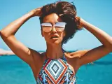 Kobieta w okularach przeciwsłonecznych na plaży, z rękami w gorze. Jej skóra ma piękny, złocisty odcień, jakby świadczył o wspaniałych beta karoten efektach.