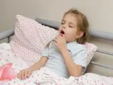 Mała dziewczynka z **przewlekłym kaszlem u dziecka** leży w łóżku, trzymając termometr.