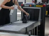 Kobieta wkłada torebkę na taśmociąg przy bramkach bezpieczeństwa. Zastanawiasz się, czy można wnieść alkohol w bagażu podręcznym? Sprawdź przepisy lotniskowe.