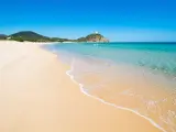 Piękne plaże Cagliari z turkusową wodą i piaszczystym brzegiem. W oddali widać wzgórze z wieżą.